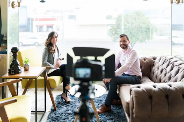 Two professionals seated on a couch during a filmed interview in a modern studio