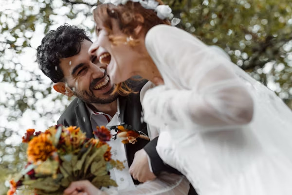 Joyful bride and groom laughing together surrounded by flower petals